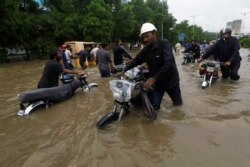 FILE - People with their motorbikes wade through the flooded road in Karachi, Pakistan, Aug. 27, 2020.