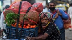 A daily wage worker carries sacks of vegetables on a bicycle during early morning in Mumbai on Feb. 1, 2022.