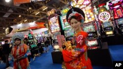 FILE - Models pose in front of slot machines at the Global Gaming Expo Asia in Macau, China, June 8, 2011. Japan's parliament passed a law on Thursday to legalize casinos, ending 15 years of political wrangling and opening the door to major investments.