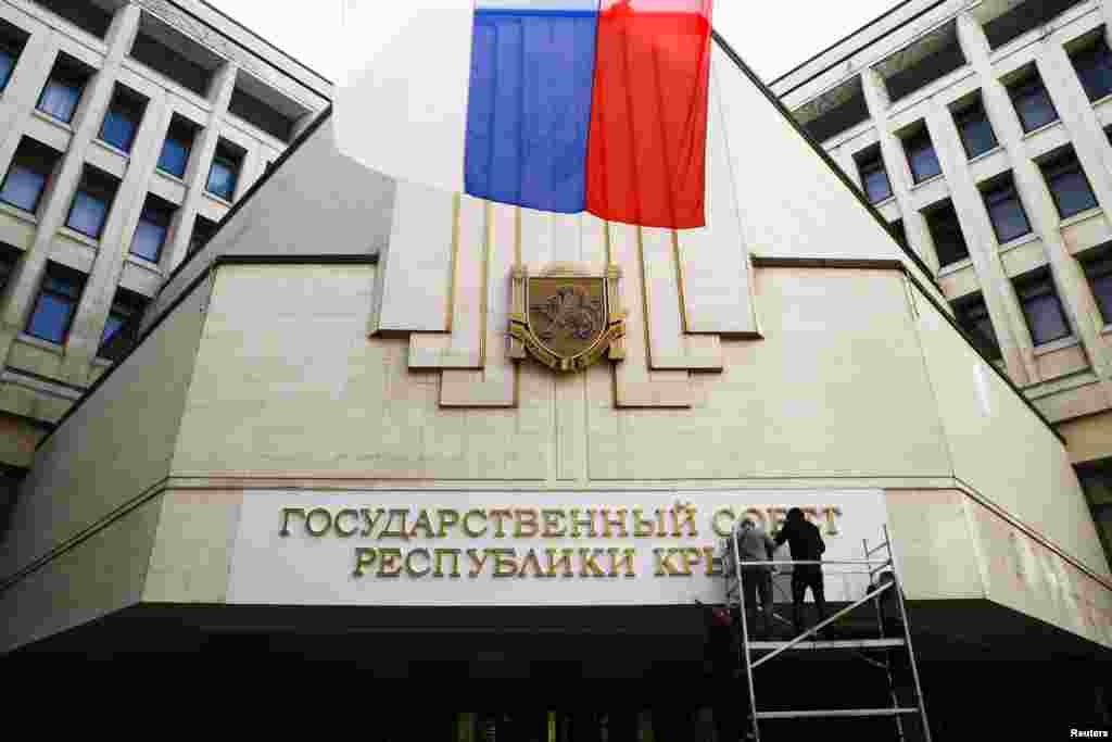 Para pekerja memasang huruf-huruf bertuliskan &quot;Dewan Negara Republik Krimea&quot; di gedung parlemen di Simferopol (19/3).&nbsp;(Reuters/Thomas Peter)