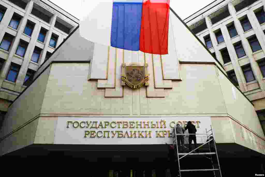 Workers put up a new sign reading "State Council of the Crimean Republic" at the parliament building in Simferopol, March 19, 2014.