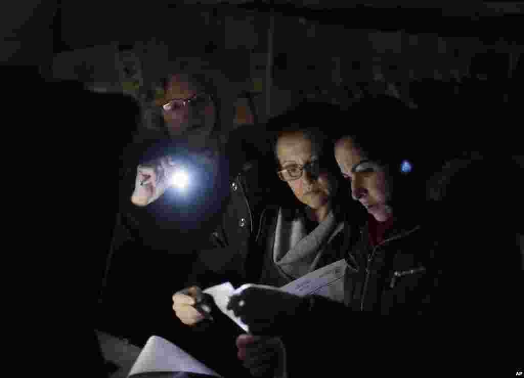 Poll workers Eva Prenga, right, Roxanne Blancero, center, and Carole Sevchuk try to start an optical scanner voting machine in the cold and dark at a polling station in a tent in the Midland Beach section of Staten Island, New York, November 6, 2012. The original polling site, a school, was damaged by Superstorm Sandy.