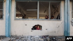 Niños palestinos miran desde un agujero en una escuela de la ONU que alberga a desplazados y que resultó dañada durante el bombardeo israelí en Khan Yunis el 21 de junio de 2024, en el sur de la Franja de Gaza, en medio del conflicto entre Israel y Hamás.