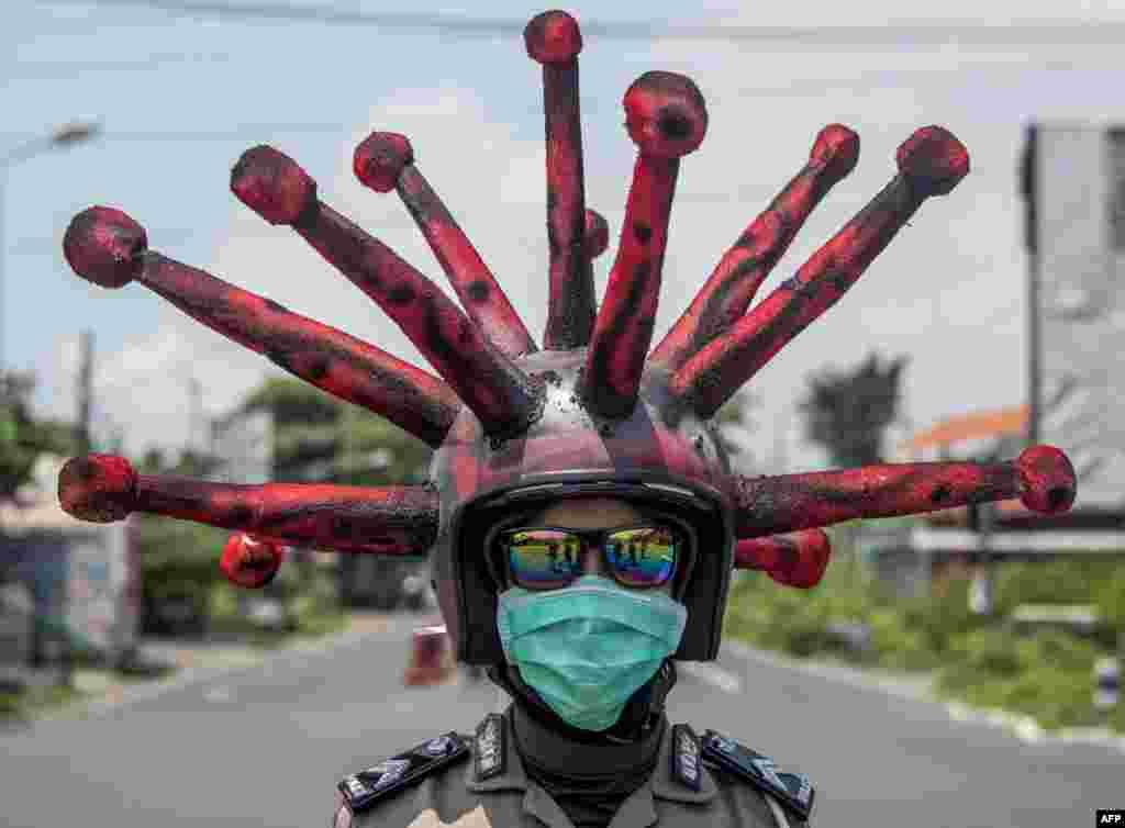 An Indonesian police officer wearing a COVID-19 coronavirus themed helmet conducts a campaign and disinfects motorists&#39; vehicles in Mojokerto, East Java.