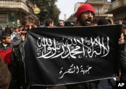 FILE - Anti-Syrian President Bashar Assad protesters hold the Jabhat al-Nusra flag, as they shout slogans during a demonstration, in Kafranbel, Idlib province, northern Syria, March 1, 2013.