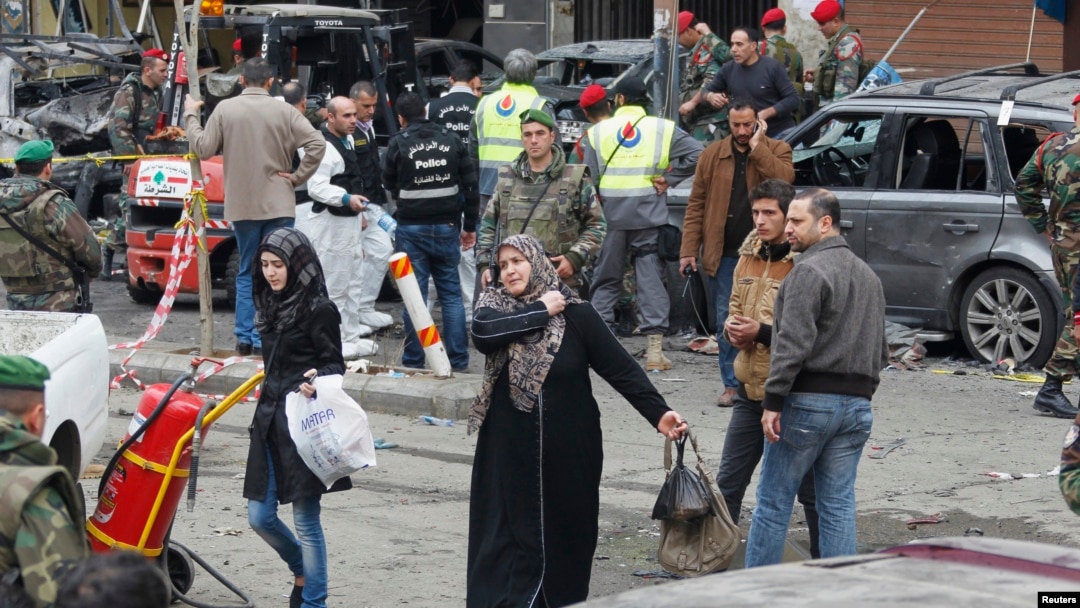 Women walk past as Lebanese army soldiers, gather at the site of Tuesday's explosion, in the Haret Hreik area in the southern suburbs of the Lebanese capital Beirut, Jan. 22, 2014.