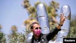 Musician Ringo Starr wears a face mask as he poses in front of his sculpture to celebrate his 80th birthday during the outbreak of the coronavirus disease (COVID-19), in Beverly Hills, California, July 7, 2020. 