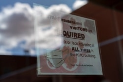 FILE - A sign on a door warns people to wear face coverings, at the Kayenta Health Center on the Navajo reservation in Kayenta, Arizona, April 18, 2020.