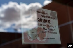 FILE - A sign on a door warns people to wear face coverings, at the Kayenta Health Center on the Navajo reservation in Kayenta, Arizona, April 18, 2020.