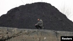 FILE - A North Korean man sits beside a pile of coal on the bank of the Yalu River in the North Korean town of Sinuiju.