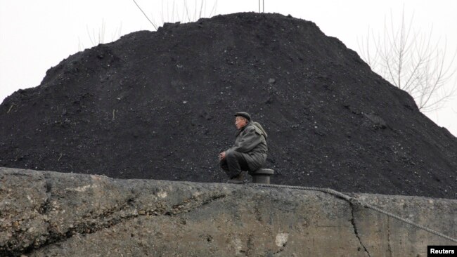FILE - A North Korean man sits beside a pile of coal on the bank of the Yalu River in the North Korean town of Sinuiju.