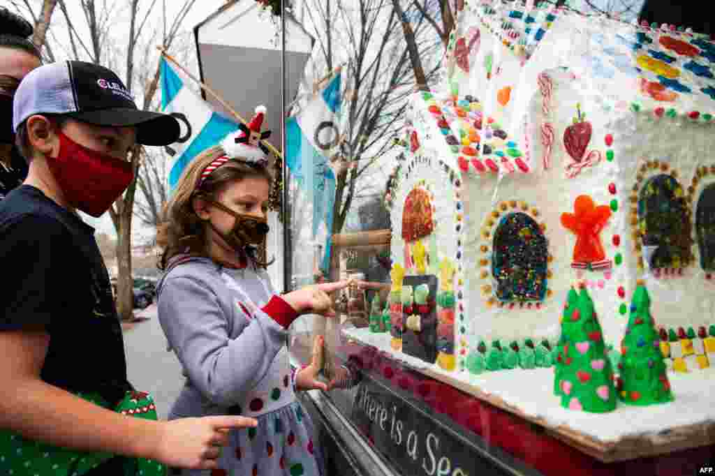 Dos ni&#241;os disfrutan viendo las decoraciones navide&#241;as, incluida una casa de pan de jengibre gigante, en los escaparates de la tienda Country en Main Street en Stockbridge, Massachusetts, el 13 de diciembre de 2020. [AFP] 