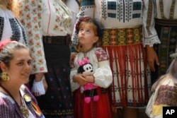 FILE - Miriam, wearing a traditional Romanian outfit, clutches her Minnie Mouse doll while posing in a group photo during a walk celebrating national outfits in various parts of the country, in Bucharest, Romania on June 20, 2020. (AP Photo/Andreea Alexandru)