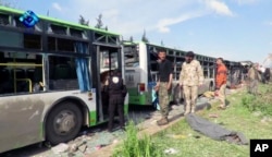 This frame grab from video provided by the Thiqa News Agency, shows rebel gunmen stand at the site of a blast that damaged several buses carrying evacuees, at the Rashideen area, outside Aleppo, Syria, April. 15, 2017.