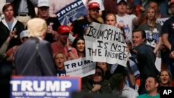 FILE - Republican presidential candidate Donald Trump, left, looks on as one of his supporter reaches for a sign that reads "Islamophobia is not the answer," at a rally in Oklahoma City, Feb. 26, 2016.