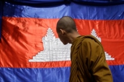 FILE- A Cambodian Buddhist monk looks at his national flag as it displays in advance of the New Year's celebration, in Phnom Penh, Cambodia, Tuesday, April 4, 2017.