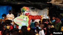 FILE - A man dressed as a clown distributes face masks to children in a slum area, amidst the coronavirus outbreak, in Mumbai, India, May 3, 2021.