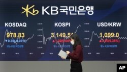 A currency trader passes by monitors showing the Korea Composite Stock Price Index, and foreign exchange rate at the foreign exchange dealing room of a KB Kookmin Bank branch in Seoul, South Korea, Jan. 14, 2021.