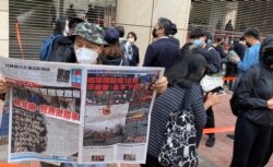 手持香港《苹果日报》的香港市民梁先生在西九法院大楼外排队，他形容防疫限聚令使香港成为一个大监狱，3月1日逾千人排队声援47名被控国安法的民主派人士有如”放监” (美国之音/汤惠芸)