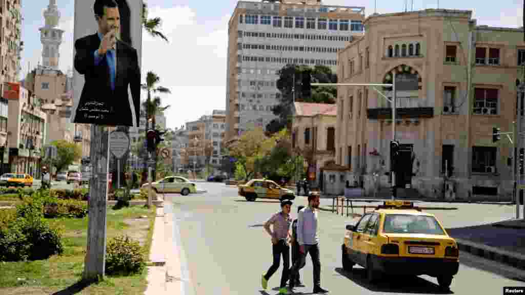 People cross a street past a poster depicting Syria's President Bashar al-Assad, in Damascus, Syria April 7, 2017.