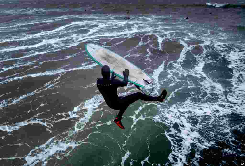 A surfer jumps into the storm-beaten Baltic Sea from the pier in Timmendorfer Strand, Germany, as temperatures reached 2&#176; C.