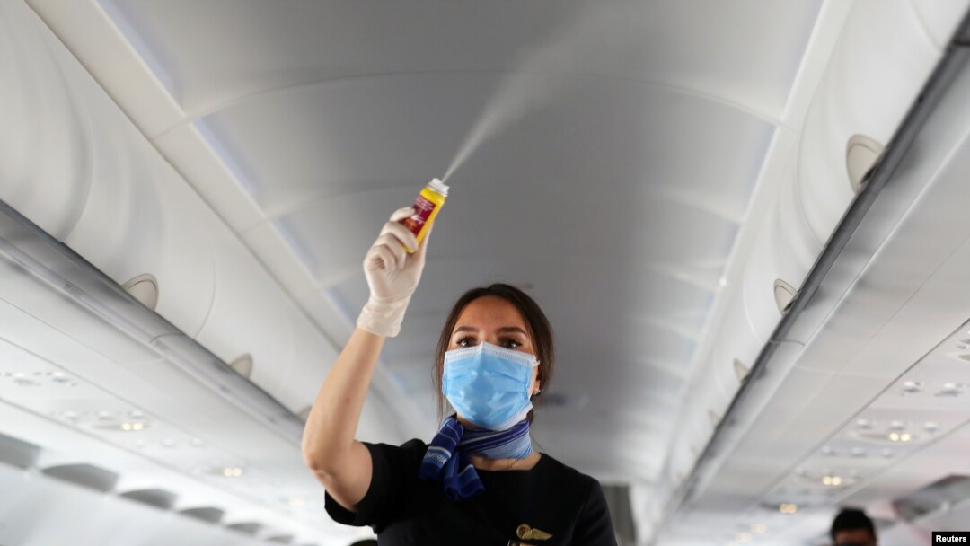 Una aeromoza usando tapabocas aplica desinfectante dentro de un avión en el aeropuerto internacional de Sharm el-Sheikh, Egipto. Junio 20, 2020.