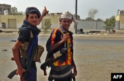 A member of the Yemeni pro-government forces (L) points to smoke in the air as he walks with another on the eastern outskirts of Hodeida as they continue in their effort to wrestle control of the city from Houthi rebels, Nov. 10, 2018.