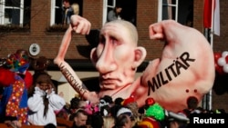 A carnival float with a caricature of Russian President Vladimir Putin moves past revelers during a carnival parade in Dusseldorf, Germany, Feb. 16, 2015. The text on the right arm reads "military;" the text on its left arm - "economy."
