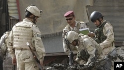 Security force personnel inspect a destroyed car at the scene of a car bomb attack in Baghdad, Iraq, Sunday, May 22, 2011