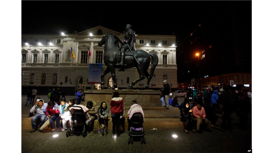 Residents sent running into the street after a magnitude-8.3 earthquake sit next to an equestrian statue in the main square of Santiago, Chile, Sept. 16, 2015.
