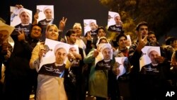 FILE - Iranians hold posters of President Hassan Rouhani, while welcoming Iranian nuclear negotiators upon their arrival from Geneva at Mehrabad Airport in Tehran Nov. 24, 2013.