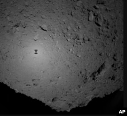 This image provided by the Japan Aerospace Exploration Agency (JAXA), shows the shadow, center left, of Japanese unmanned spacecraft Hayabusa2 over the asteroid Ryugu Friday, Sept. 21, 2018. (JAXA via AP)