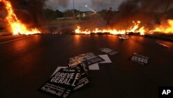 Military policemen clear a flaming barricade on an access highway to Brasilia, Brazil, June 30, 2017. Signs that read in Portuguese "General strike" are strewn on the road.