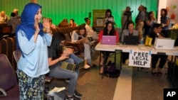 While activists and lawyers at the table at right offer help and information, Hanadi Al-Haj prays in the Tom Bradley International Terminal at Los Angeles International Airport as she waits for her Yemeni mother to arrive, June 29, 2017, in Los Angeles, C