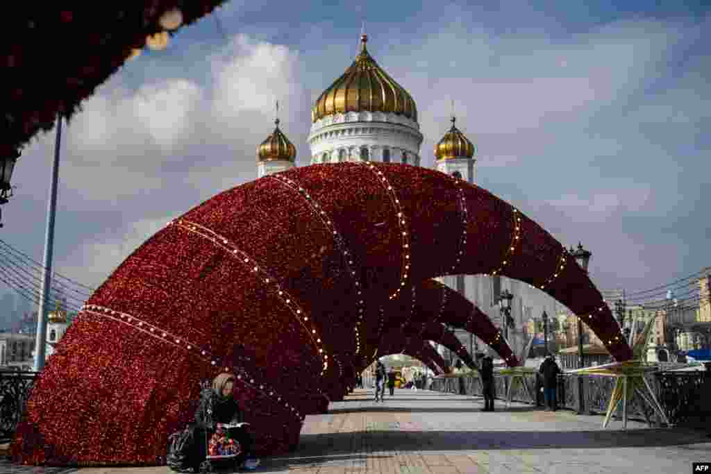 An elderly woman sells traditional Russian wooden nesting dolls, called Matryoshka dolls, on a bridge over the Moskva river in front of the Cathedral of Christ the Saviour in downtown Moscow.