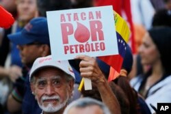 A man holds a sign that reads in Spanish "They attack for oil" during a march of in support of the state-run oil company PDVSA, in Caracas, Venezuela, Jan. 31, 2019.