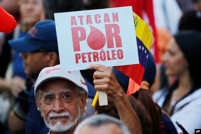 A man holds a sign that reads in Spanish "They attack for oil" during a march of in support of the state-run oil company PDVSA, in Caracas, Venezuela, Jan. 31, 2019.