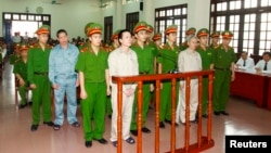 Doan Van Vuon (standing, 4th L), Doan Van Quy (standing, 2nd L) and Doan Van Sinh (standing, 3rd R) stand with policemen in front of the dock at a court during a verdict session in Hai Phong, April 5, 2013.