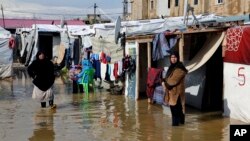 FILE - Syrian refugees stand in a pool of mud and rain water at a refugee camp, in the town of Bar Elias, in the Bekaa Valley, Lebanon, Jan. 10, 2019.