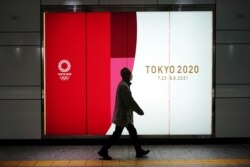 FILE - A man wearing a protective mask to help curb the spread of the coronavirus walks near a banner of the Tokyo 2020 Olympics at an underpass in Tokyo, Jan. 19, 2021.