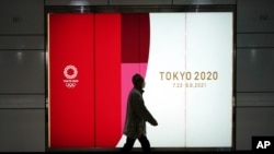 A man wearing a protective mask to help curb the spread of the coronavirus walks near a banner of the Tokyo 2020 Olympics at an underpass in Tokyo, Jan. 19, 2021. (AP photo/Eugene Hoshiko)