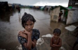 In this June 26, 2014 photo, a girl, self-identified as Rohingya, stands close to her family's tent house at Dar Paing camp for refugees, suburbs of Sittwe, Western Rakhine state, Myanmar.