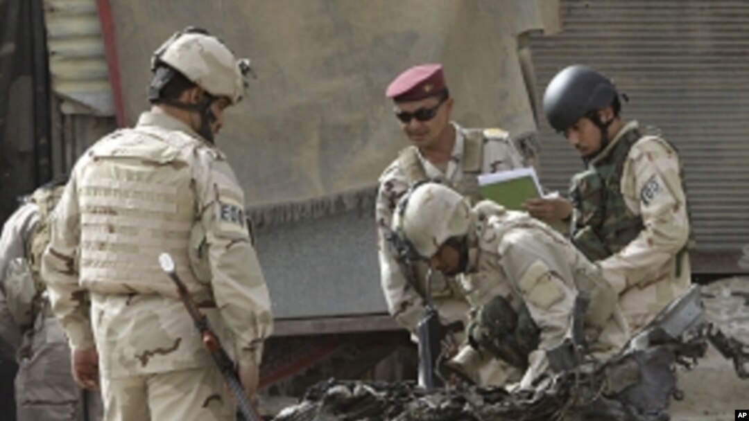Security force personnel inspect a destroyed car at the scene of a car bomb attack in Baghdad, Iraq, Sunday, May 22, 2011