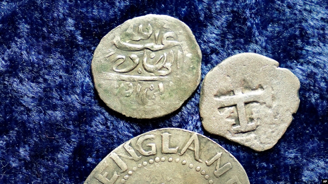 A 17th century Arabian silver coin, top, that research shows was struck in 1693 in Yemen, rests above a 1652 Massachusetts Bay Colony Oak Tree Shilling , and a 1727 Spanish half real coin, on a table, in Warwick, Rhode Island, March 11, 2021.