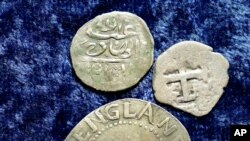 A 17th century Arabian silver coin, top, that research shows was struck in 1693 in Yemen, rests above a 1652 Massachusetts Bay Colony Oak Tree Shilling , and a 1727 Spanish half real coin, on a table, in Warwick, Rhode Island, March 11, 2021.