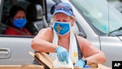 Usando una mascarilla en medio de preocupaciones por el coronavirus, la voluntaria Karen Cooperstein descarga galones de leche para donar al público durante un evento de donación de alimentos de Catholic Charities, en Dallas, Texas, el 2 de julio de 2020.