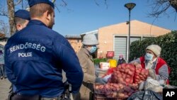 Police officers patrolling to control the observance of lockdown regulations introduced by the Hungarian government to contain the pandemic of coronavirus watch a customer buying vegetables at a market in the city centre of Szeged, Hungary, April 6, 2020.