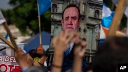 Los manifestantes sostienen una pancarta con el retrato del presidente guatemalteco Alejandro Giammattei durante una protesta por la reelección de Consuelo Porras como fiscal general, Ciudad de Guatemala, el sábado 21 de mayo de 2022.