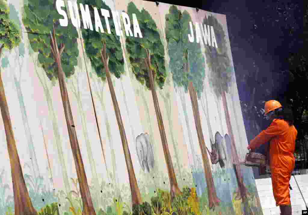 A Greenpeace activist uses a chainsaw to cut down a wooden wall symbolizing Indonesian forests during a demonstration against deforestation in Jakarta, Indonesia. (AP Photo/Tatan Syuflana)