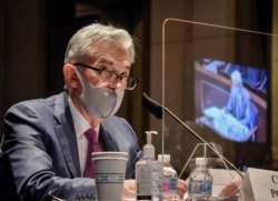 FILE - Federal Reserve Board Chairman Jerome Powell, reflected in the sneeze guard set up between himself and members of the House Committee on Financial Services, speaks during a hearing on Capitol Hill, June 30, 2020.
